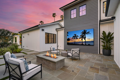 A large wall-mounted outdoor TV on a stone patio in front of a modern house.