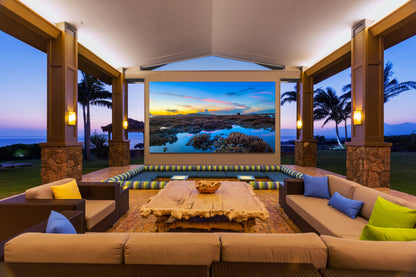 A luxury outdoor movie lounge setup on a covered patio, featuring a large dvLED display, surrounded by sectional sofas.
